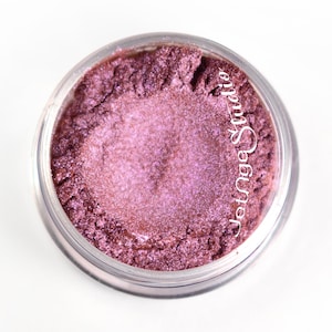 May include: A jar of shimmering, deep rose-colored eyeshadow. The powder has a metallic sheen and is contained in a clear plastic jar. The text "Jetnge Studio" is printed on the side of the jar.