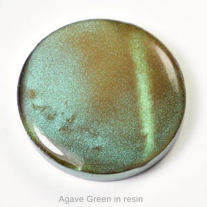 May include: A circular resin piece with a colour gradient of agave green and gold. The surface has a speckled, glittery appearance. The text "Agave Green in resin" is at the bottom of the image.