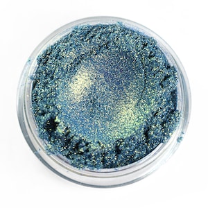 May include: A small round jar of teal blue eyeshadow with a shimmery finish.