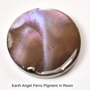 May include: A round, metallic-looking resin piece with a shimmering, iridescent effect. The colors shift from brown to purple and blue, with the text "Earth Angel Ferro Pigment in Resin" at the bottom. The piece has a glossy finish.