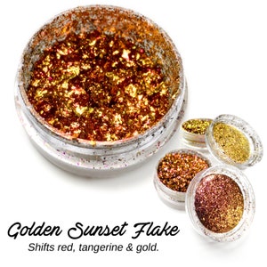 May include: Golden Sunset Flake glitter in a clear jar. The glitter is a mix of red, gold, and orange flakes. The text "Golden Sunset Flake" and "Shifts red, tangerine & gold." is printed below the jar.