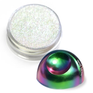 Puede incluir: Un pequeño frasco de purpurina blanca iridiscente con una esfera iridiscente verde, azul y púrpura a su lado. La esfera tiene una pequeña hendidura en la parte superior.