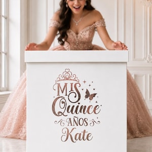 Op de afbeelding: Een witte vierkante doos met roségouden metallic tekst en afbeeldingen. Het ontwerp bevat een tiara, een vlinder en de woorden Mis Quince Años Kate. De doos heeft een strakke esthetiek met een gladde afwerking en een deksel aan de bovenkant.