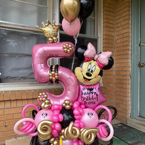 May include: A pink number 5 balloon with a gold crown on top, surrounded by pink, gold, and black balloons. A Minnie Mouse balloon with a pink bow is next to the number 5. The balloons are arranged in a bouquet shape. The text "Happy Birthday Desiree" is on a pink balloon.