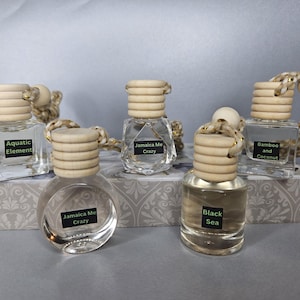 May include: Five small glass bottles with wooden tops and string hangers. The bottles contain different scented liquids. The labels on the bottles read "Aquatic Element", "Jamaica Me Crazy", "Bamboo and Coconut", and "Black Sea".