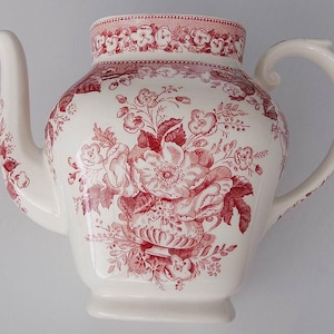 May include: A white ceramic teapot with a red floral pattern. The teapot has a spout and a handle.