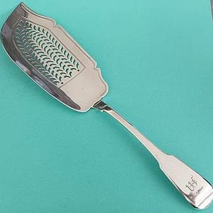 May include: A silver fish server with a slotted blade featuring a decorative leaf design. The handle has a monogrammed initial. The server is approximately 11 inches long.