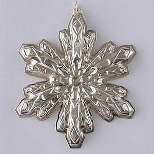 May include: A silver snowflake ornament with a detailed, intricate design. The snowflake has six points and is made of metal.
