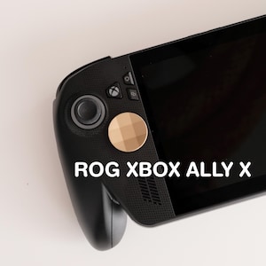 May include: A black ROG XBOX ALLY X handheld gaming console. The device features a black body, a screen, and a gold-coloured button. The text "ROG XBOX ALLY X" is displayed in white.