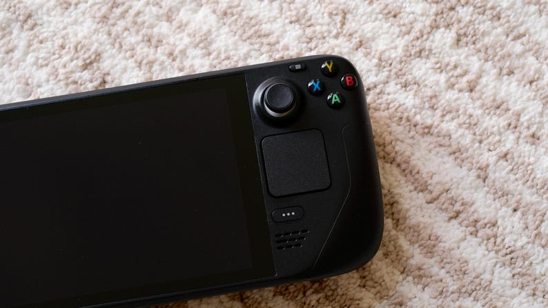 May include: A black handheld gaming console with a large screen and integrated controls. The console features a directional pad, analog stick, buttons, and a touchpad. The device is designed for portable gaming and entertainment.