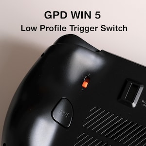 May include: Close-up of a black GPD WIN 5 handheld gaming device. The text "GPD WIN 5 Low Profile Trigger Switch" is visible. Features include an orange power indicator light and an R4 button.