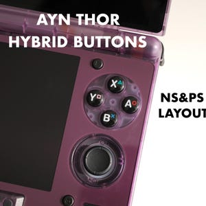 May include: A close-up of a purple handheld gaming device with the text "AYN THOR HYBRID BUTTONS" and "NS&PS LAYOUT". The device features a black screen, a circular directional pad, and a cluster of four colored buttons: X, Y, A, and B.