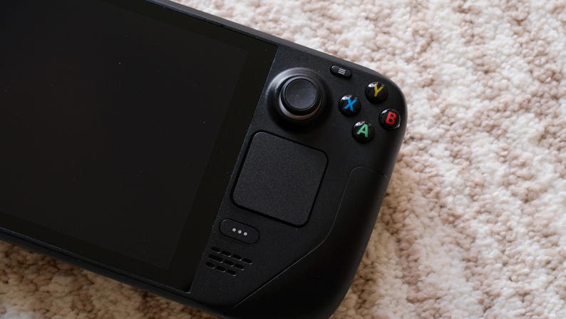 May include: Black handheld gaming console with a large screen and integrated controls. Features a joystick, directional pad, and colored action buttons. The device has a sleek, modern design.