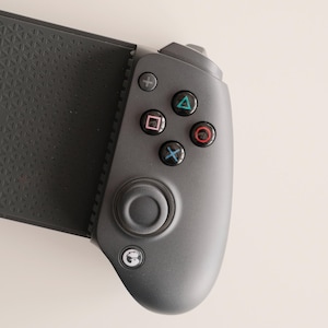 May include: A dark gray mobile gaming controller with the brand name "GameSir" printed on the textured grip. The controller features a directional pad, analog stick, and action buttons in various colors.