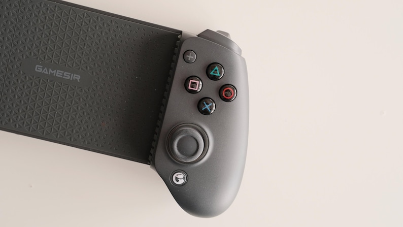 May include: A dark gray mobile gaming controller with the brand name "GameSir" printed on the textured grip. The controller features a directional pad, analog stick, and action buttons in various colors.