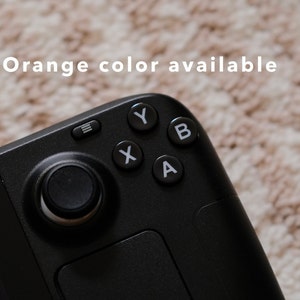 Könnte beinhalten: Ein schwarzer Handheld-Gaming-Controller mit einem runden Knopf in der Mitte, einem Touchpad und Knöpfen mit den Beschriftungen A, B, X, Y.