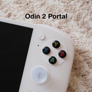 May include: Close-up of a white handheld gaming device with black buttons labeled A, B, X, and Y in green, red, blue, and yellow. The text "Odin 2 Portal" is printed on the image.