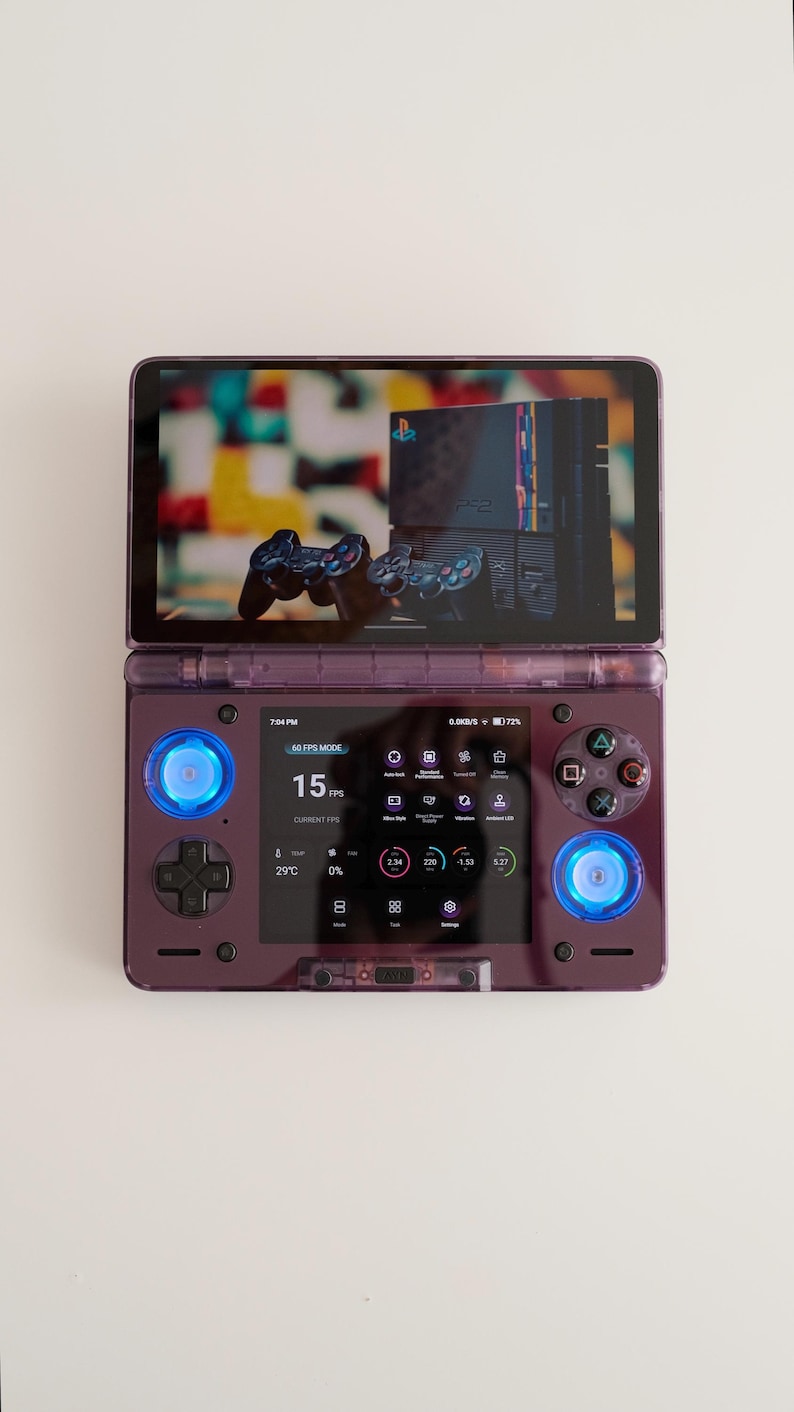May include: A purple handheld gaming console with a screen displaying a video game interface. The console has buttons, joysticks, and a D-pad. The screen shows the text "60 FPS MODE" and "15 FPS".