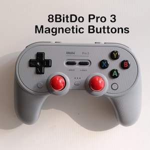 Op de afbeelding: Een grijze 8BitDo Pro 3 gamecontroller met magnetische knoppen. De controller heeft een zwart kruis, gekleurde actieknoppen en rode joysticks. De tekst "8BitDo Pro 3 Magnetic Buttons" staat bovenaan.
