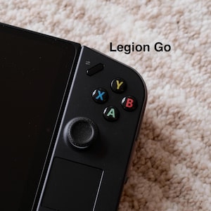 Könnte beinhalten: Nahaufnahme eines schwarzen Legion Go Handheld-Gaming-Geräts. Das Gerät verfügt über einen Bildschirm auf der linken Seite und einen Controller auf der rechten Seite mit farbigen Tasten: X (blau), Y (gelb), B (rot) und A (grün). Der Text "Legion Go" ist sichtbar.