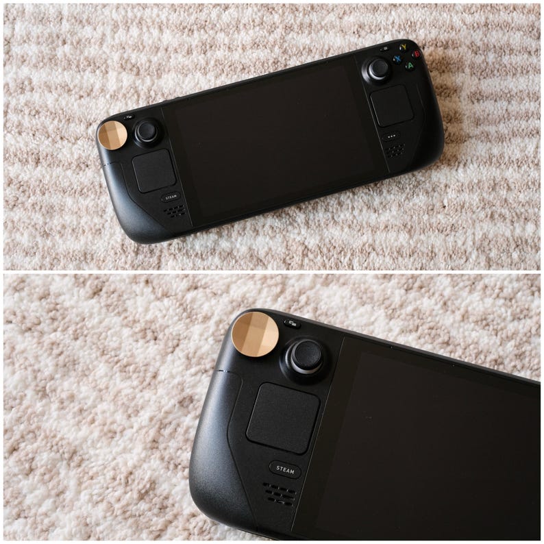 May include: A black handheld gaming console with a large screen and integrated controls. The console features a black body with a matte finish, a screen, and buttons. The joysticks have gold-colored accents. The word "STEAM" is printed on the console.