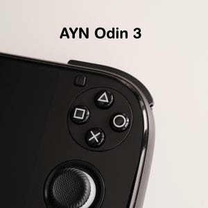 Puede incluir: Primer plano de un dispositivo de juegos portátil AYN Odin 3 negro. La imagen destaca los botones de control, incluido un panel direccional, botones de acción (triángulo, cuadrado, cruz, círculo) y una palanca analógica. El dispositivo tiene un acabado brillante.