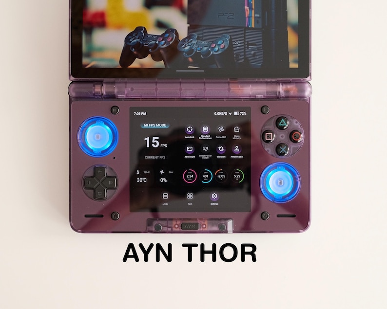 May include: A purple handheld gaming console with a screen displaying game information. The console has blue illuminated buttons and the text "AYN THOR" at the bottom. The screen shows the FPS at 15.