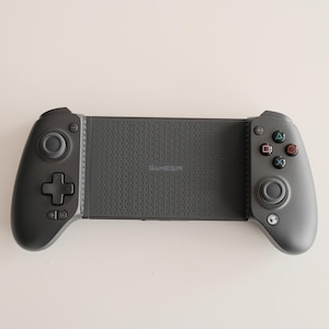 May include: A dark gray GAMESIR mobile gaming controller. The controller has a textured center section with the GAMESIR logo, and two gray handles with buttons and control sticks. The controller is designed for mobile gaming.