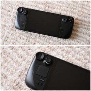 May include: A black handheld gaming console with a large screen, two thumbsticks, and various buttons. The console has a sleek, modern design and features the "STEAM" logo. The device is shown on a light-colored, textured surface.