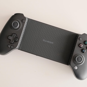 May include: A black mobile gaming controller with a textured grip and multiple buttons. The controller has a central section with the word "GameSir" printed on it, and two side grips with control sticks and buttons.