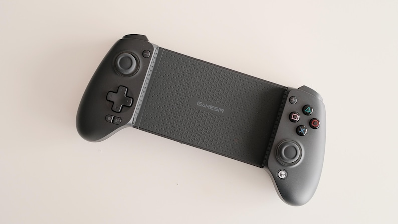 May include: A black mobile gaming controller with a textured grip and multiple buttons. The controller has a central section with the word "GameSir" printed on it, and two side grips with control sticks and buttons.