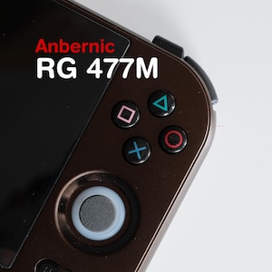 Könnte beinhalten: Nahaufnahme einer braunen Handheld-Spielkonsole mit dem Text "Anbernic RG 477M". Die Konsole verfügt über einen schwarzen Bildschirm, ein Steuerkreuz und farbige Aktionstasten.