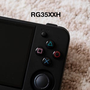 May include: A black handheld gaming console with a screen and coloured control buttons. The buttons are blue, green, pink, and red. The text "RG35XXH" is printed at the top of the device.