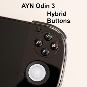 Może przedstawiać: Zbliżenie czarnej przenośnej konsoli do gier z tekstem "AYN Odin 3 Hybrid Buttons". Urządzenie posiada krzyżak, cztery kolorowe przyciski akcji (X, Y, A, B) oraz centralny drążek analogowy.