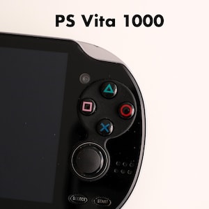 Può includere: Primo piano di una console di gioco portatile nera PS Vita 1000. La console presenta uno schermo nero, un pad direzionale con pulsanti colorati e il testo "PS Vita 1000" in alto. I pulsanti includono un triangolo verde, un cerchio rosso, una X blu e un quadrato rosa.