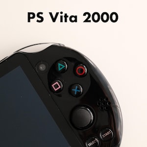 Może przedstawiać: Zbliżenie czarnej przenośnej konsoli do gier PS Vita 2000. Konsola posiada ekran, przyciski kierunkowe i przyciski akcji w kolorach czerwonym, niebieskim, zielonym i różowym. Tekst "PS Vita 2000" jest wyświetlany powyżej.