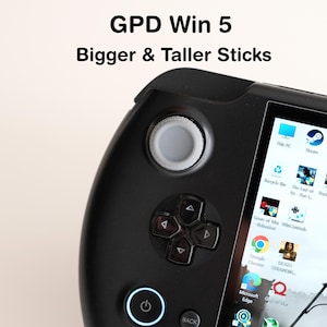 Może przedstawiać: Czarne urządzenie do gier przenośnych GPD Win 5 z tekstem "Bigger & Taller Sticks". Urządzenie posiada ekran wyświetlający ikony aplikacji, d-pad i joysticki.