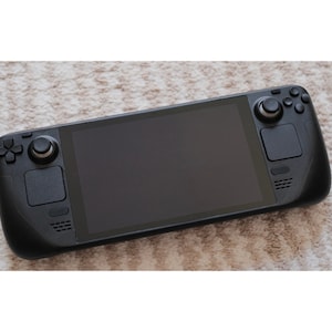 Puede incluir: Una consola de juegos portátil negra con una pantalla grande, dos joysticks analógicos y varios botones.