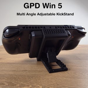 Op de afbeelding: Zwarte GPD Win 5 handheld gaming-apparaat met een multi-hoek verstelbare kickstand. Het apparaat staat op een houten oppervlak. De tekst "GPD Win 5" en "Multi Angle Adjustable KickStand" zijn zichtbaar.