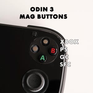 May include: Close-up of a black handheld gaming device with the text "ODIN 3 MAG BUTTONS." The device features a directional pad with A and B buttons, and a joystick. The text "XBOX, PS, GC, SFC" is also visible.
