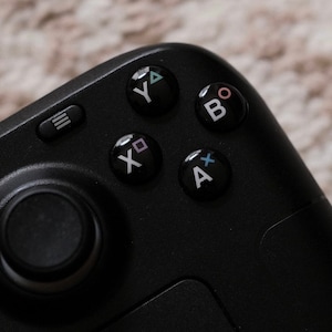 May include: A black gaming controller with a circular joystick, four buttons labelled "A", "B", "X", and "Y", and a button with three horizontal lines.