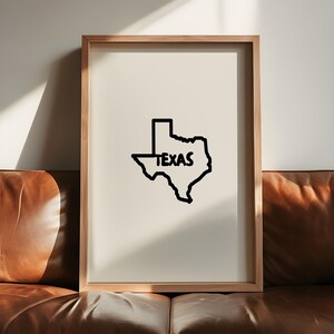 May include: A framed print featuring a black outline of the state of Texas with the word "TEXAS" in the center. The artwork is set against a cream-colored background and framed in a light wood.