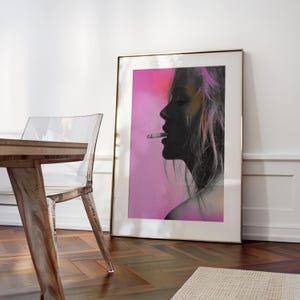 May include: A framed art print featuring a side profile silhouette of a person smoking a cigarette. The artwork has a pink and orange gradient background. The frame is gold-colored, and the print is displayed against a white wall.