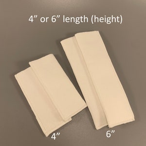 May include: Two white fabric strips, one 4 inches long and the other 6 inches long.  The fabric strips are folded in half and sewn together at the edges.  4" or 6" length (height)