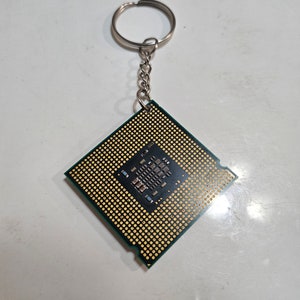 May include: A green and gold computer chip keychain with a silver chain and ring.