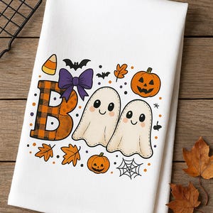 May include: White Halloween-themed towel with the word "BOO" in orange and black plaid, and two smiling ghost characters. The design includes pumpkins, bats, leaves, a spider web, and candy corn.