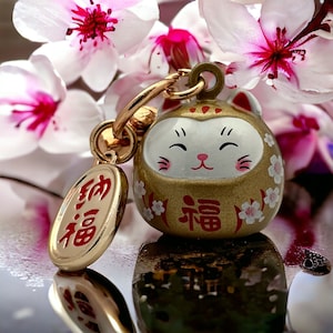 May include: Gold charm featuring a white cat face and the Japanese word "福" (meaning "good fortune") on the front. The charm is attached to a gold chain and has a small oval tag with the Japanese word "幸福" (meaning "happiness") on it.