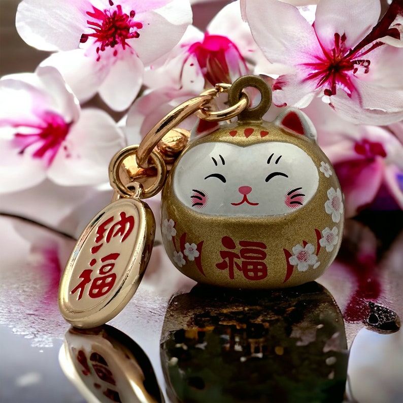 May include: Gold charm featuring a white cat face and the Japanese word "福" (meaning "good fortune") on the front. The charm is attached to a gold chain and has a small oval tag with the Japanese word "幸福" (meaning "happiness") on it.