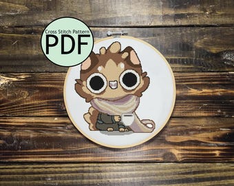 Puede incluir: Patrón de punto de cruz PDF para un gato de dibujos animados marrón y blanco que lleva una bufanda y sostiene una taza. El gato tiene ojos grandes y redondos y una expresión amigable.