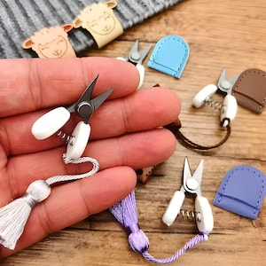 May include: A set of five small, colorful, leather-wrapped scissors with white handles. The scissors are perfect for small craft projects and are a great addition to any sewing kit.